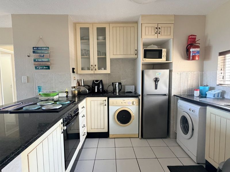 Functional kitchen featuring cream cabinetry, granite countertops, built-in oven and hob, and integrated laundry facilities with tiled flooring and backsplash.