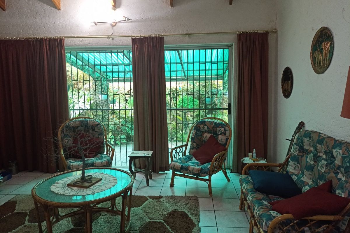 A living room featuring exposed timber ceiling beams, tiled flooring, and large sliding glass doors with security bars leading to an outdoor area.