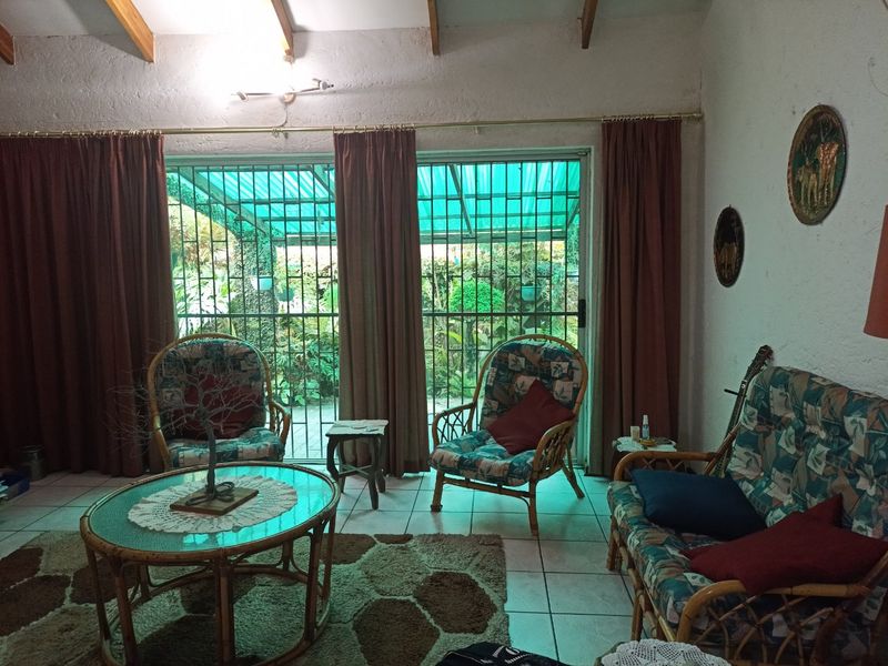 A living room featuring exposed timber ceiling beams, tiled flooring, and large sliding glass doors with security bars leading to an outdoor area.