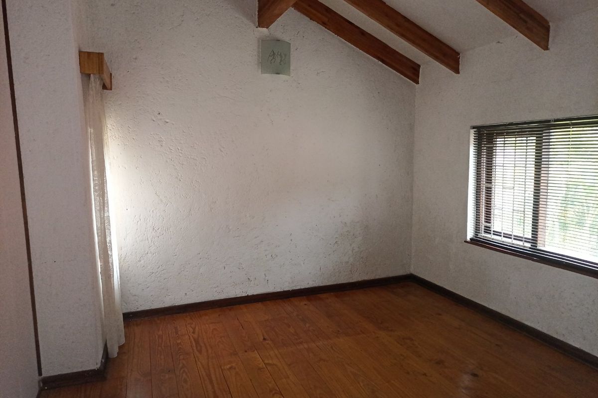 An empty bedroom featuring exposed timber ceiling beams, polished timber flooring, and textured walls with venetian blinds.