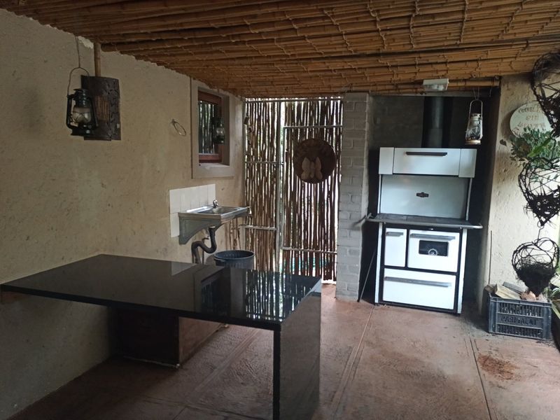 Covered outdoor patio area featuring a built-in stove, granite prep counter, and wall-mounted sink under a rustic bamboo ceiling.
