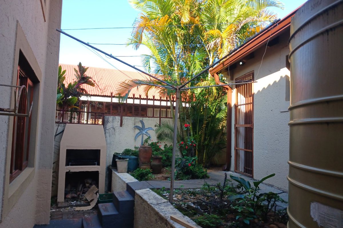 Rear courtyard area featuring a built-in braai, water storage tank, and established garden beds with paved pathways.