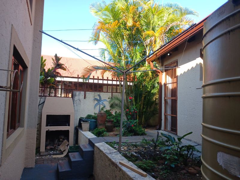 Rear courtyard area featuring a built-in braai, water storage tank, and established garden beds with paved pathways.