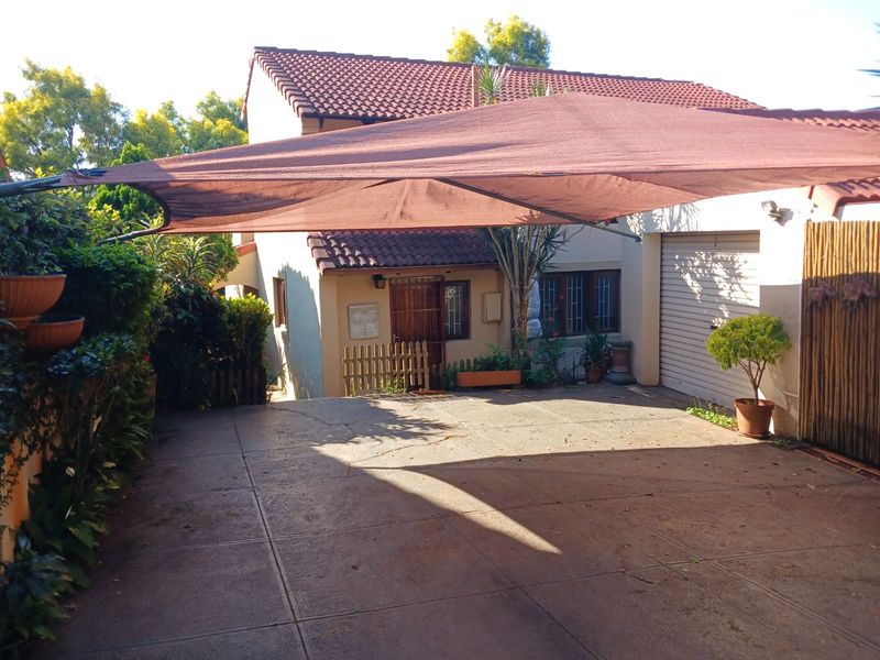Front exterior view of the property featuring a paved driveway, garage, and a shade sail structure over the parking area.