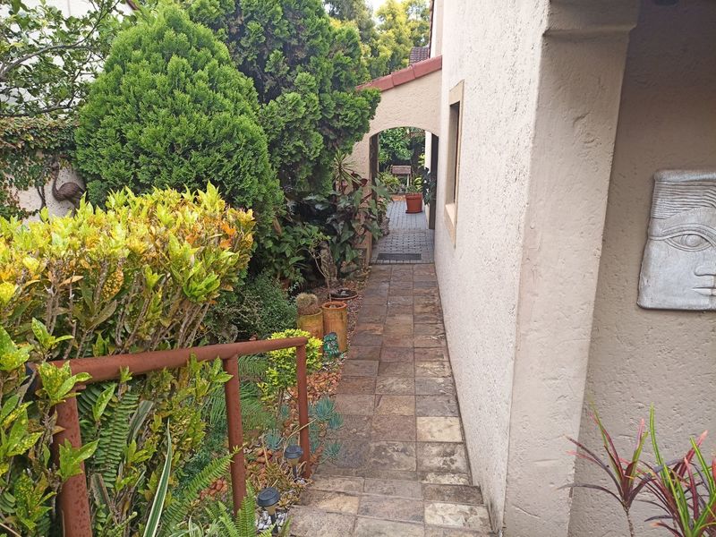 A paved exterior walkway featuring an arched passage, stucco wall finish, and mature garden landscaping along the side of the property.