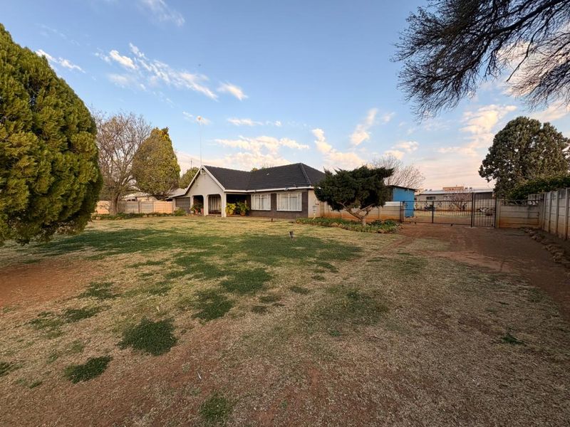 Front view of a single-story house featuring a tiled roof, covered entrance porch, and a large front garden with a gated driveway entrance.