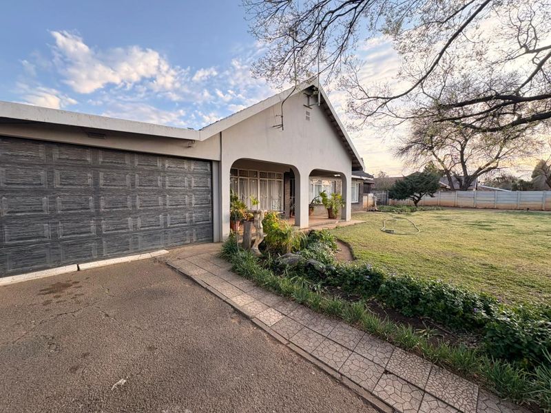 Front view of the property featuring a paved driveway, attached garage, covered patio area, and a well-maintained lawn with boundary wall.