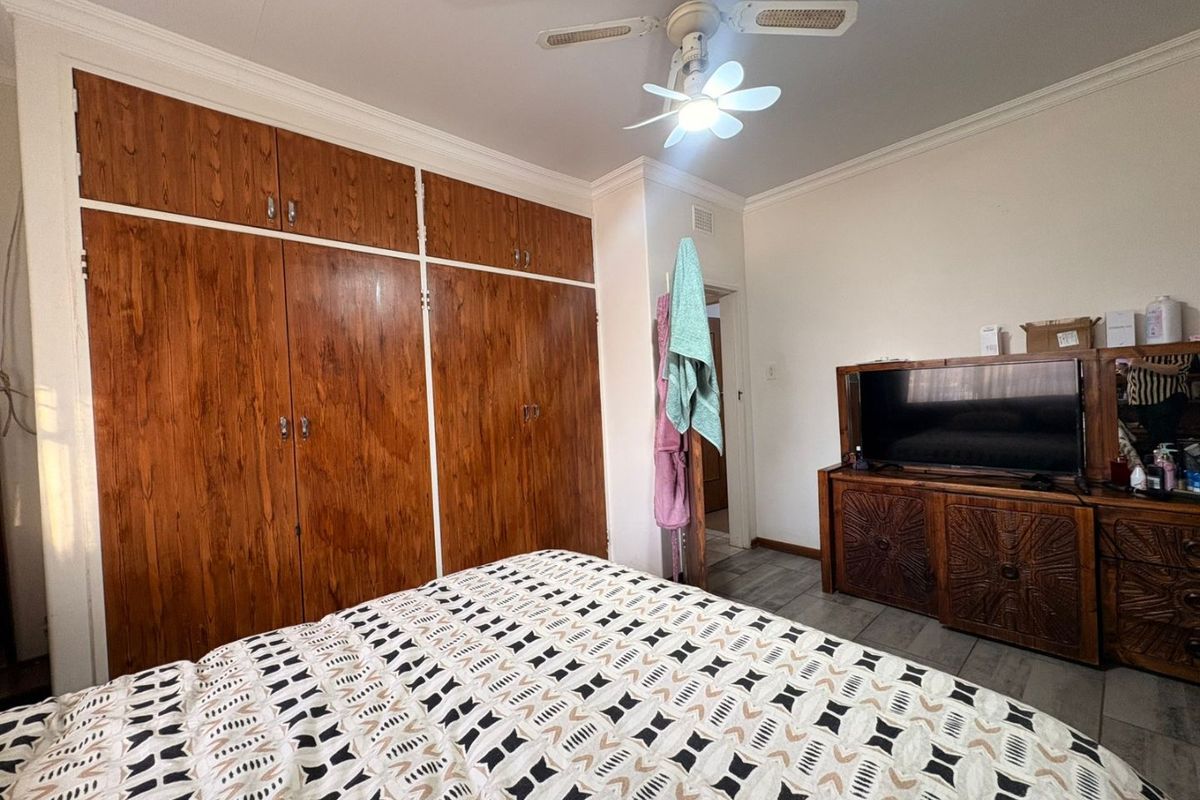 A bedroom featuring extensive built-in wooden cupboards, a ceiling fan, and coving detail.