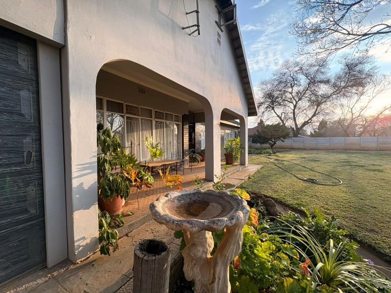A spacious covered patio featuring arched columns and tiled flooring, providing a seamless transition to the expansive rear garden.