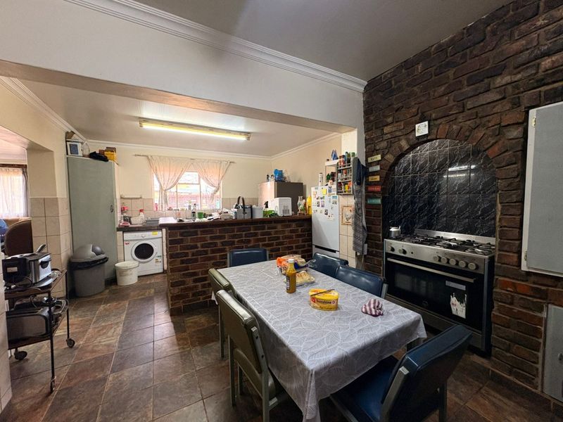 Open-plan kitchen and dining area featuring a rustic brick feature wall, built-in oven, gas hob, and tiled flooring with integrated laundry plumbing.