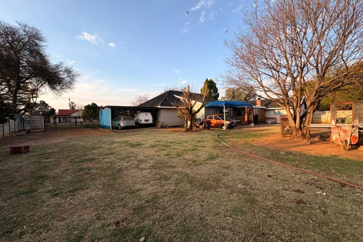 A spacious rear garden area featuring a carport, established trees, and a view of the main house structure with a tiled roof.