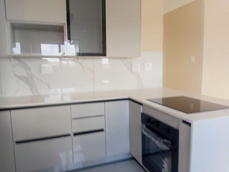 Modern kitchen featuring sleek gloss cabinetry, quartz countertops, a marble-look splashback, and integrated electric oven and hob.