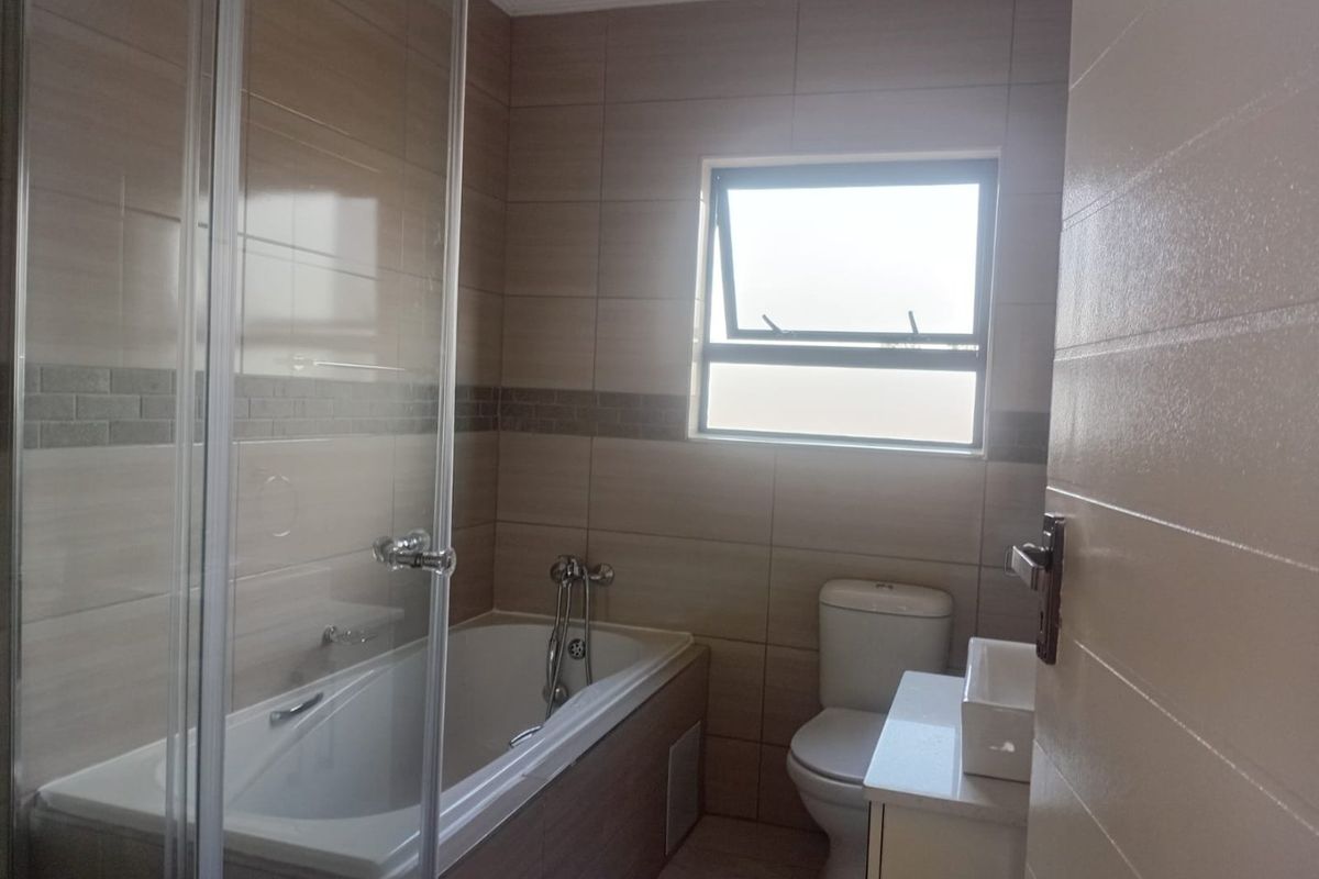 A clean, modern bathroom featuring a built-in bathtub, separate glass shower enclosure, toilet, and a vanity basin with neutral wall tiling.