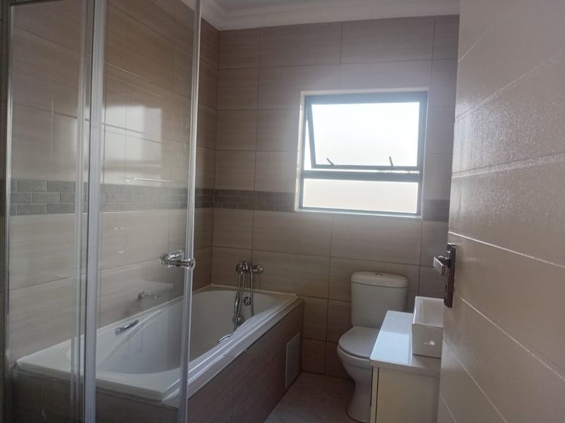 A clean, modern bathroom featuring a built-in bathtub, separate glass shower enclosure, toilet, and a vanity basin with neutral wall tiling.