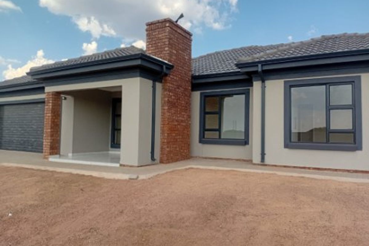Front elevation of a modern house featuring a brick chimney, tiled roof, and dark aluminium window frames with an unlandscaped front yard.