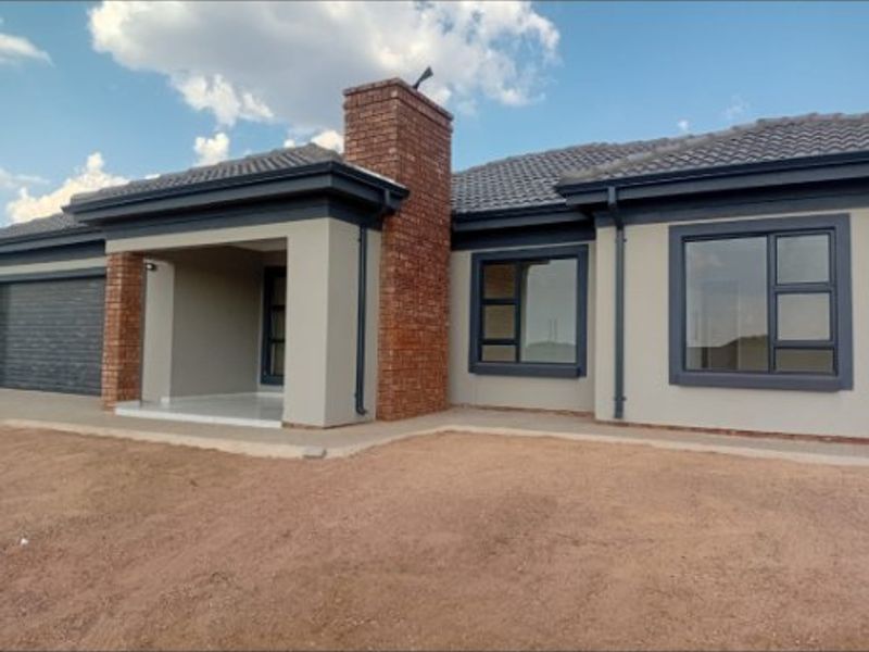 Front elevation of a modern house featuring a brick chimney, tiled roof, and dark aluminium window frames with an unlandscaped front yard.