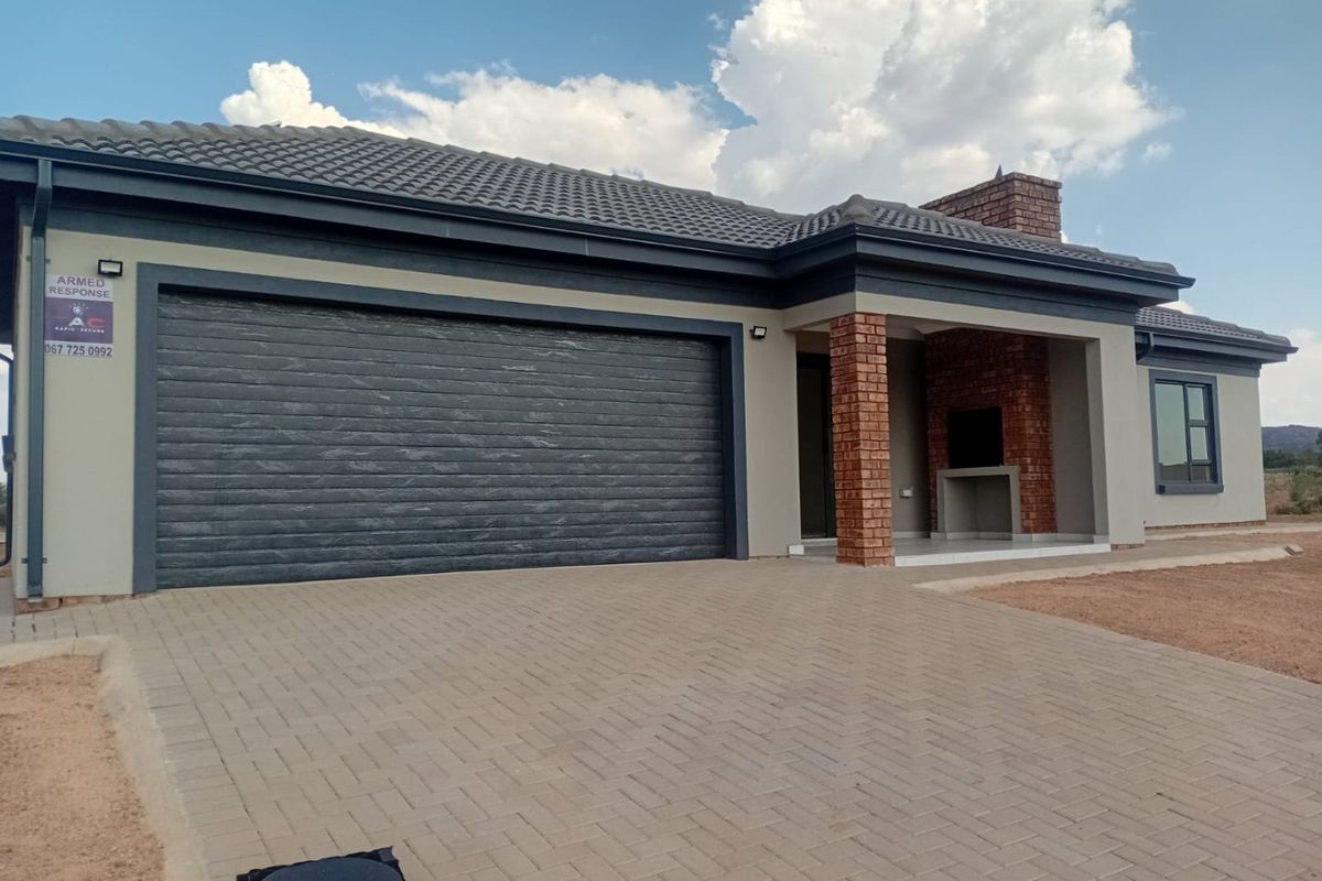 Modern single-story home featuring a double garage, paved driveway, and a covered patio area with a built-in brick braai.