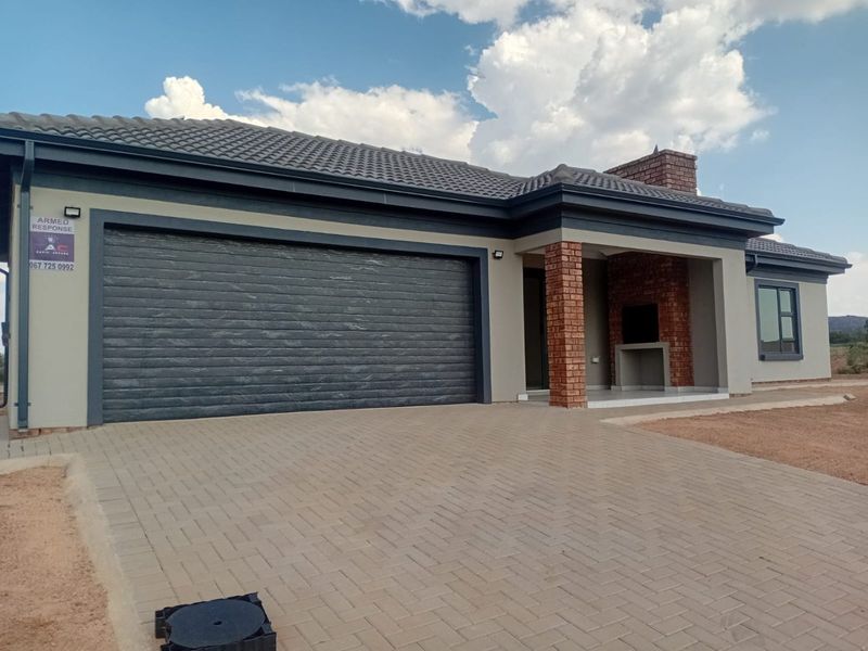 Modern single-story home featuring a double garage, paved driveway, and a covered patio area with a built-in brick braai.