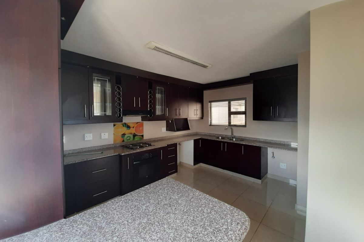 A spacious kitchen featuring dark wood cabinetry, granite countertops, a built-in oven, gas hob, and tiled flooring, offering a functional and well-maintained workspace.