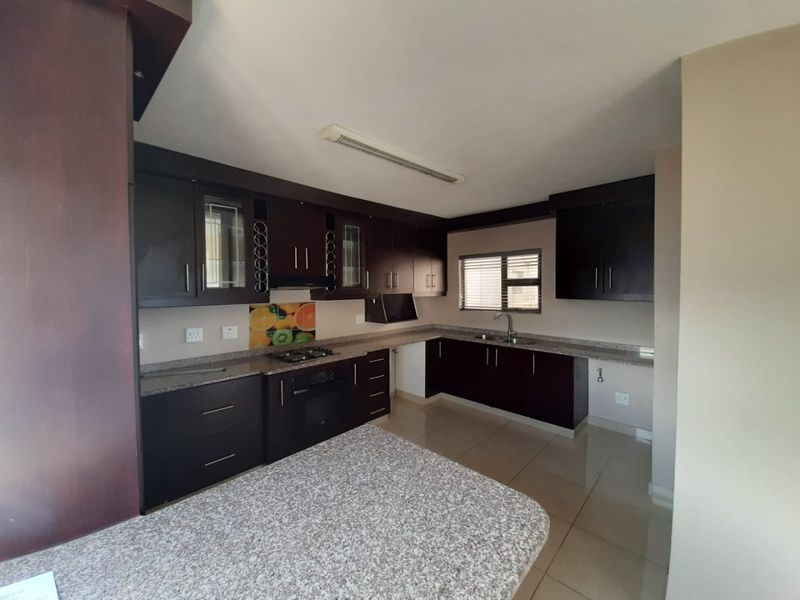 A spacious kitchen featuring dark wood cabinetry, granite countertops, a built-in oven, gas hob, and tiled flooring, offering a functional and well-maintained workspace.