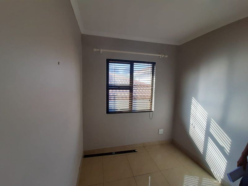 A clean, empty bedroom featuring neutral wall paint, tiled flooring, and a window fitted with venetian blinds.