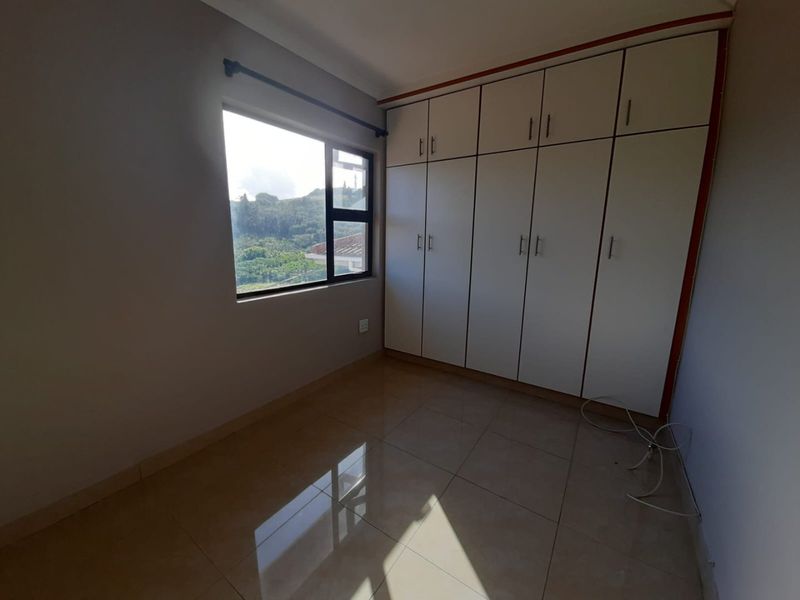 A bright, empty bedroom featuring neutral tiled flooring and extensive floor-to-ceiling built-in cupboards, offering ample storage space and natural light.