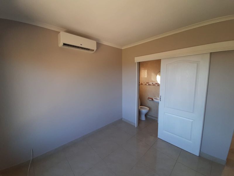 A spacious, empty bedroom featuring tiled flooring, a wall-mounted air conditioning unit, and direct access to an en-suite bathroom via a sliding door.