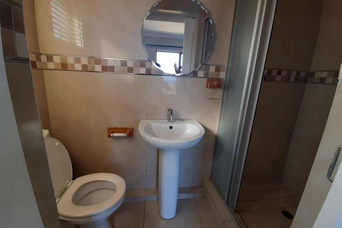 A functional bathroom featuring a pedestal basin, toilet, and a separate shower enclosure with neutral ceramic wall and floor tiling.