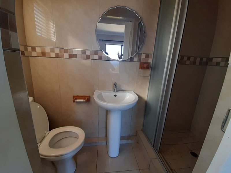 A functional bathroom featuring a pedestal basin, toilet, and a separate shower enclosure with neutral ceramic wall and floor tiling.