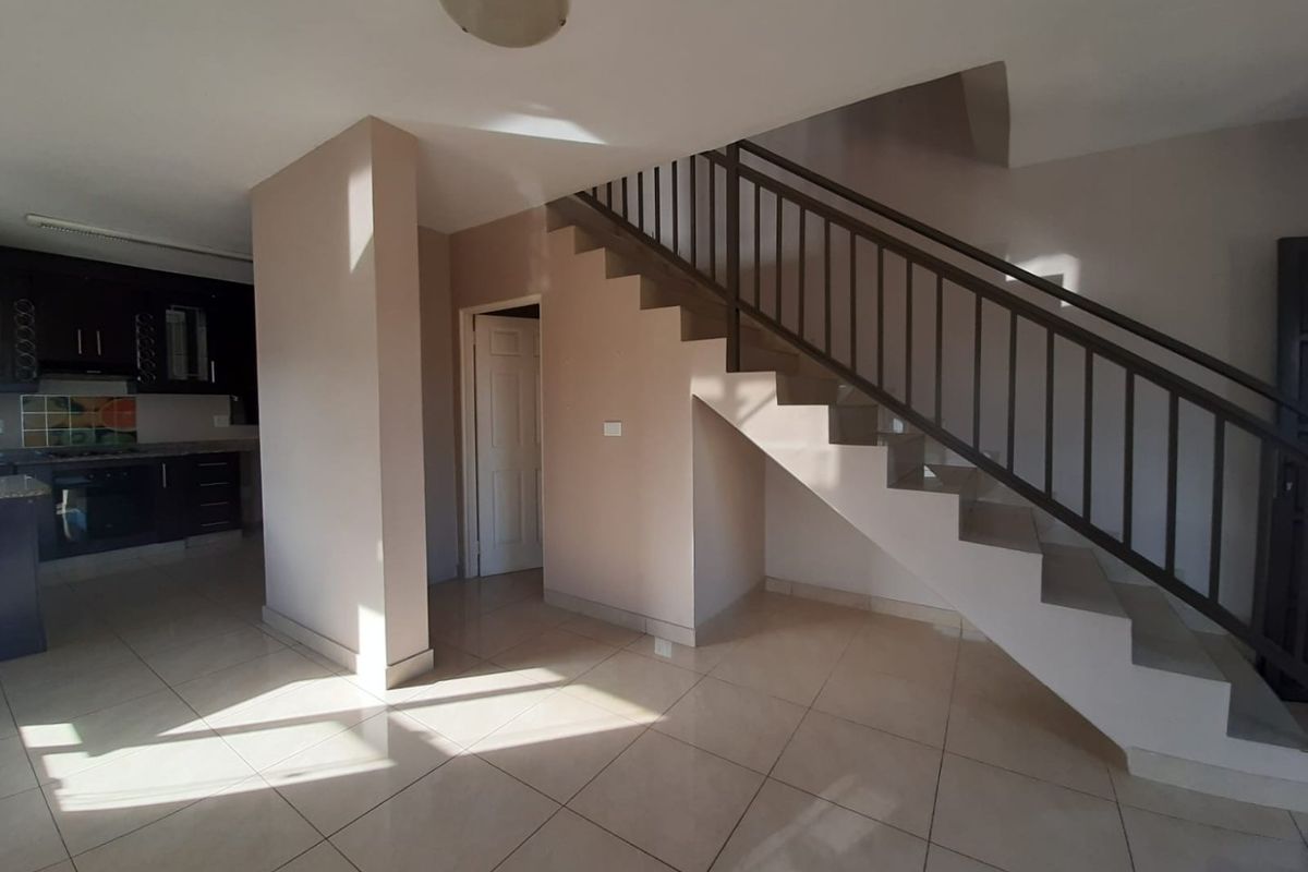 Open plan living area featuring a staircase with metal balustrade, tiled flooring, and an adjacent kitchen with built-in cabinetry and appliances.