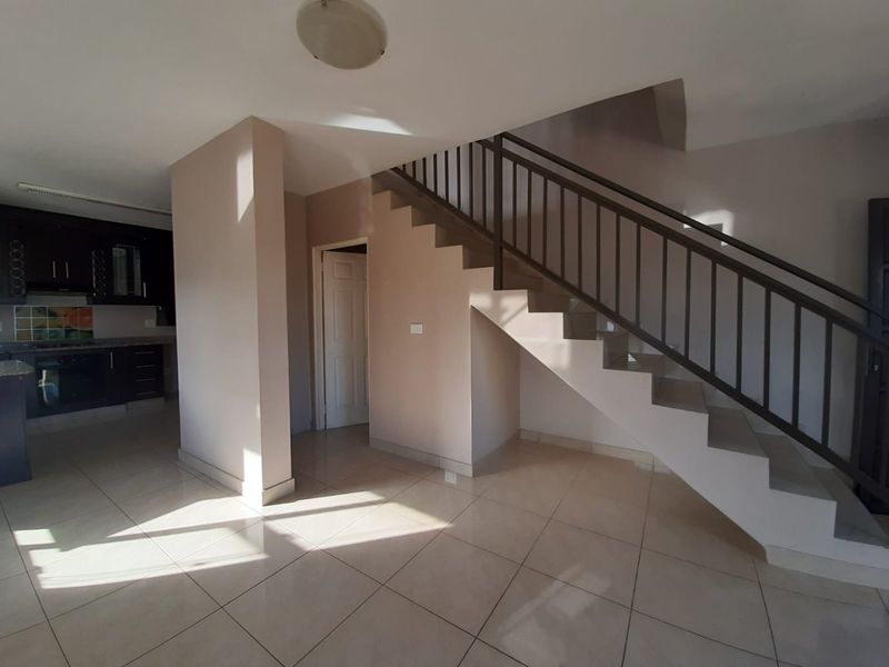 Open plan living area featuring a staircase with metal balustrade, tiled flooring, and an adjacent kitchen with built-in cabinetry and appliances.