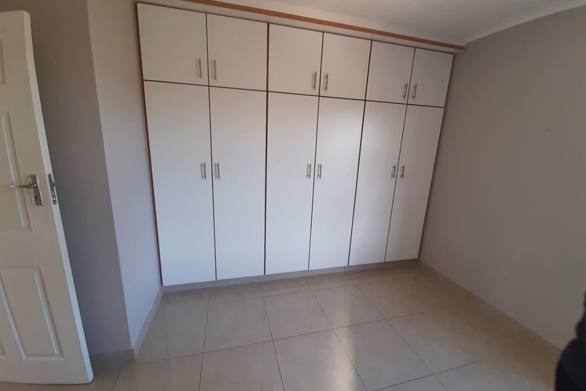 A clean, empty bedroom featuring neutral tiled flooring and extensive white built-in cupboards providing ample storage space.