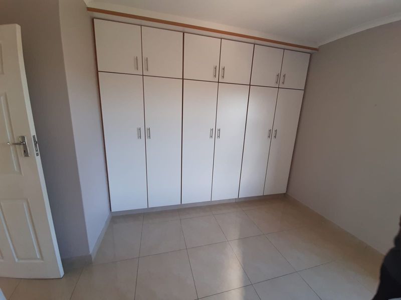 A clean, empty bedroom featuring neutral tiled flooring and extensive white built-in cupboards providing ample storage space.