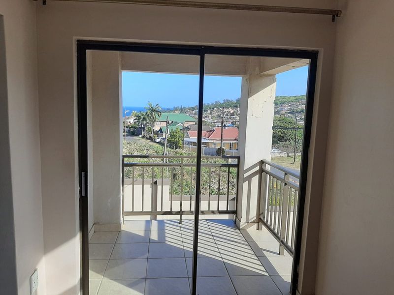 A covered balcony featuring tiled flooring, a metal balustrade, and sliding glass door access, offering an elevated view of the surrounding neighbourhood.