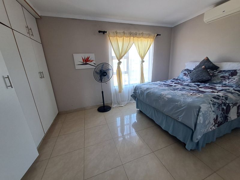 A well-maintained bedroom featuring tiled flooring, built-in cupboards, and a wall-mounted air conditioning unit.