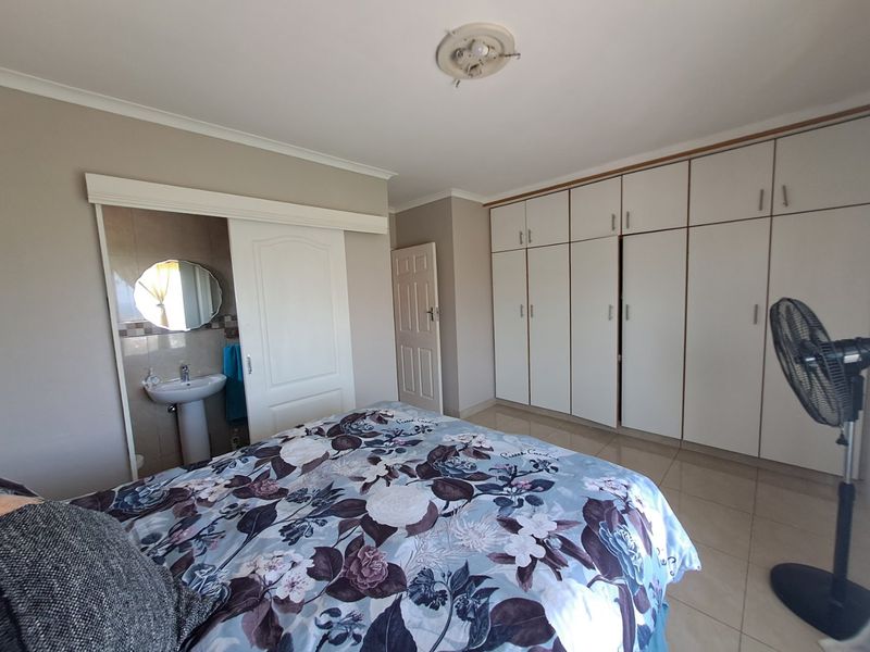 Spacious bedroom featuring extensive built-in cupboards, tiled flooring, and an integrated en-suite vanity area with a pedestal basin.
