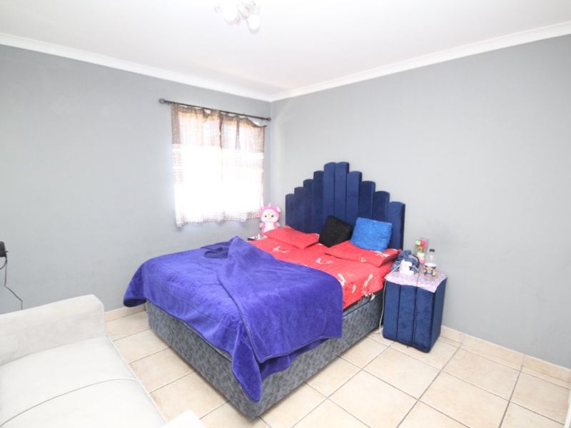 A bedroom featuring neutral grey walls, tiled flooring, and a coved ceiling, providing a functional and well-lit sleeping space.
