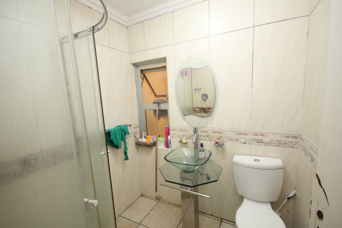 Compact bathroom featuring a glass shower enclosure, pedestal glass basin, and toilet with tiled finishes throughout.