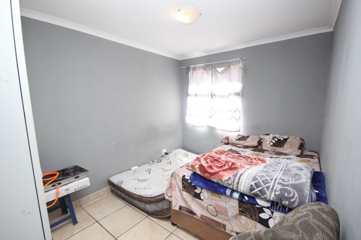 A compact bedroom featuring tiled flooring and neutral grey walls, offering a functional space with potential for cosmetic updates.