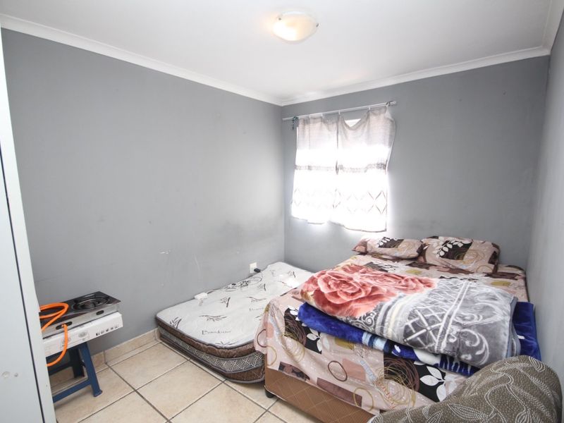 A compact bedroom featuring tiled flooring and neutral grey walls, offering a functional space with potential for cosmetic updates.