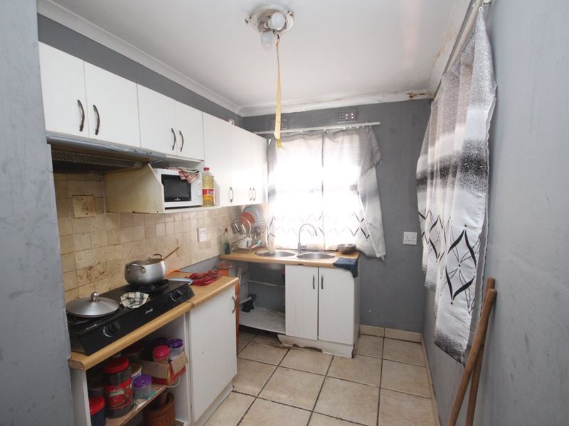 Compact kitchen featuring white cabinetry, tiled backsplash, and double sink, requiring cosmetic updates and repairs to the ceiling and cabinetry.