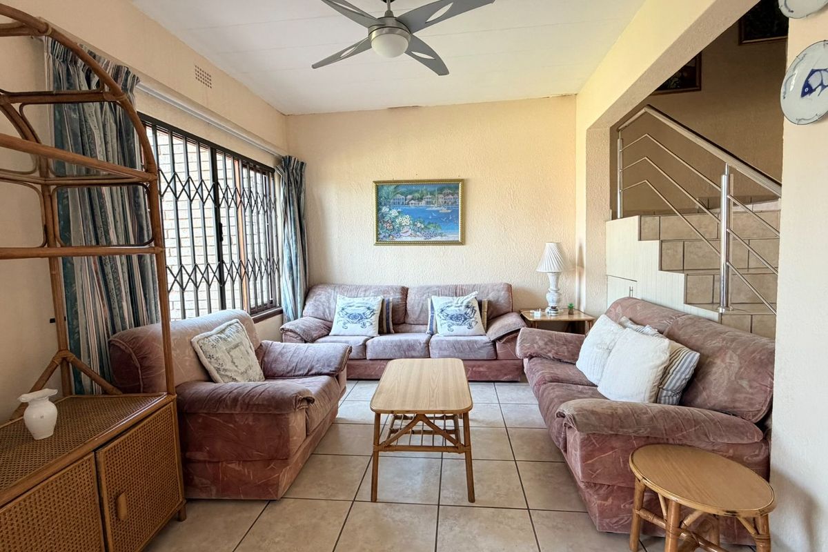 A comfortable living room featuring tiled flooring, a ceiling fan, and an internal staircase with a modern metal railing.