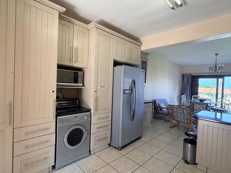Open-plan kitchen and living area featuring neutral built-in cabinetry, granite countertops, tiled flooring, and direct access to an outdoor patio space.