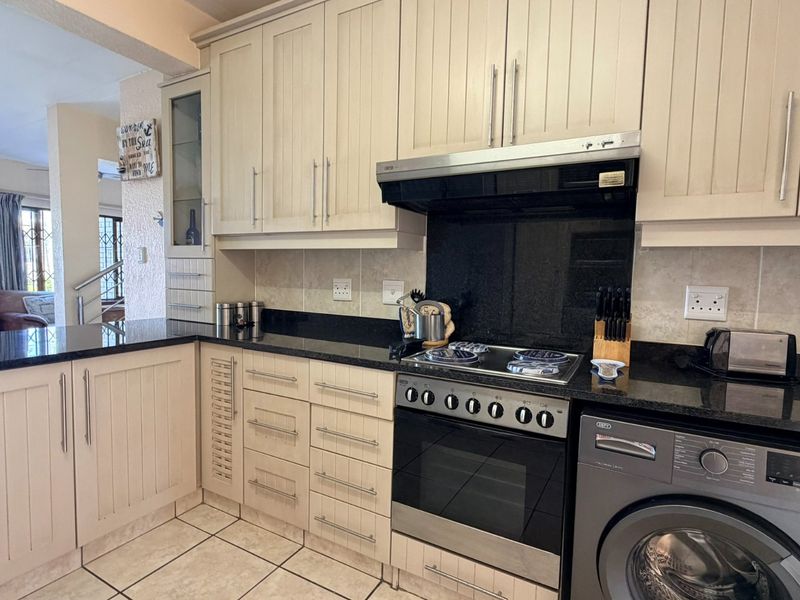 A functional kitchen featuring cream-colored cabinetry, black granite countertops, a built-in oven and stove, and tiled flooring, with an open-plan layout.