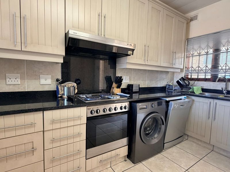 A functional kitchen featuring light-toned cabinetry, granite countertops, a built-in oven with hob, and tiled finishes throughout.