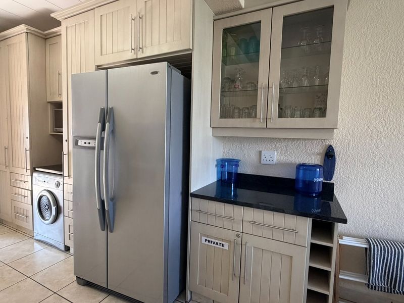 A functional kitchen area featuring cream-colored cabinetry, dark granite countertops, glass-fronted display units, and tiled flooring with an integrated washing machine.