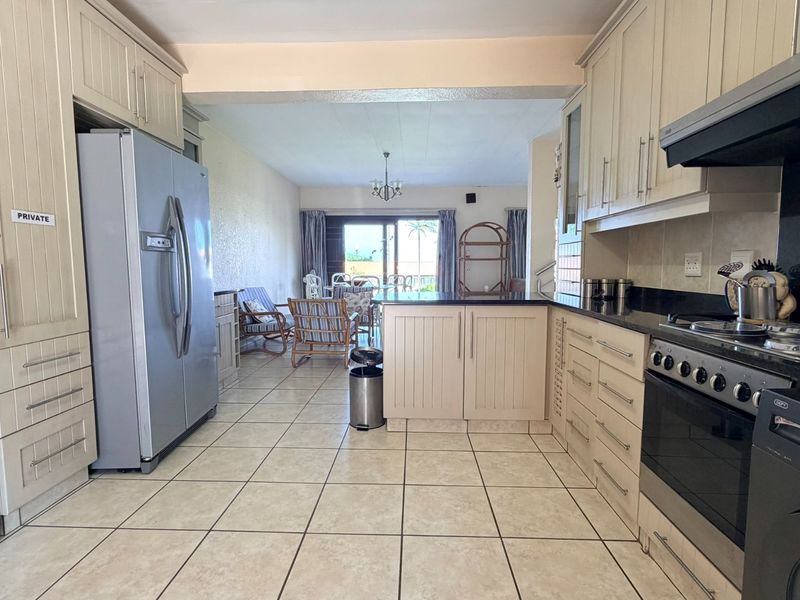 Open-plan kitchen and living area featuring neutral cabinetry, granite countertops, tiled flooring, and direct access to a patio through sliding glass doors.