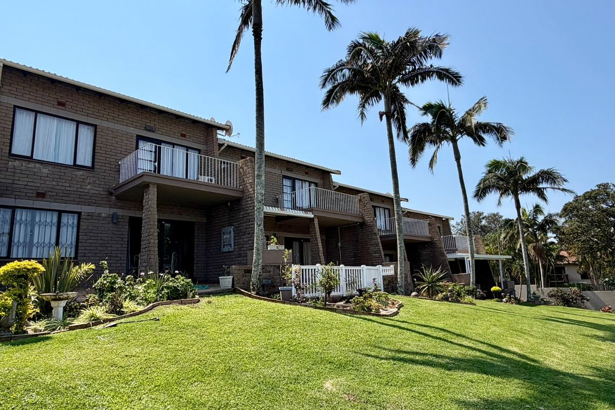 Rear view of a multi-story townhouse complex featuring face brick construction, private balconies with metal railings, and a well-maintained communal lawn area.