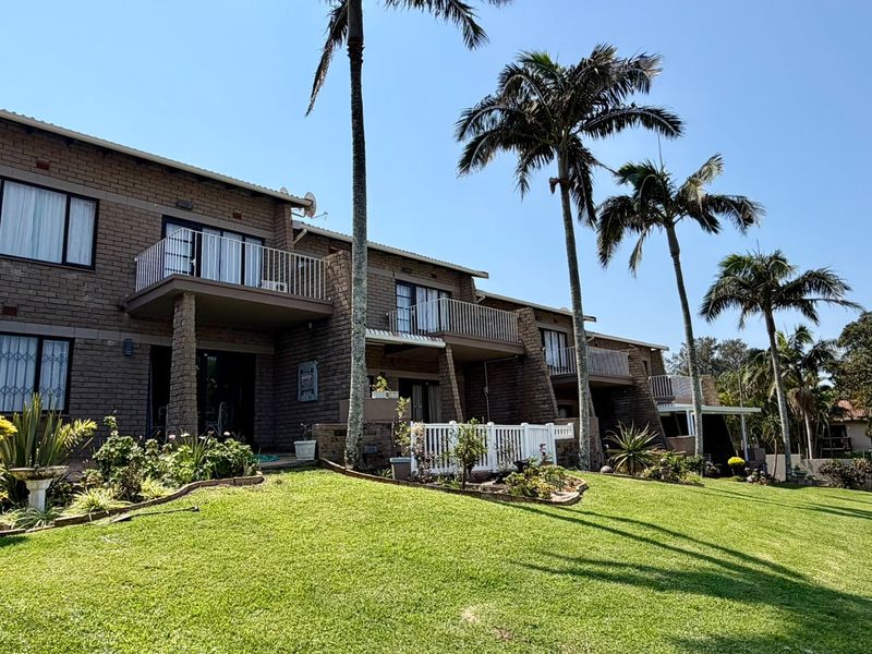 Rear view of a multi-story townhouse complex featuring face brick construction, private balconies with metal railings, and a well-maintained communal lawn area.