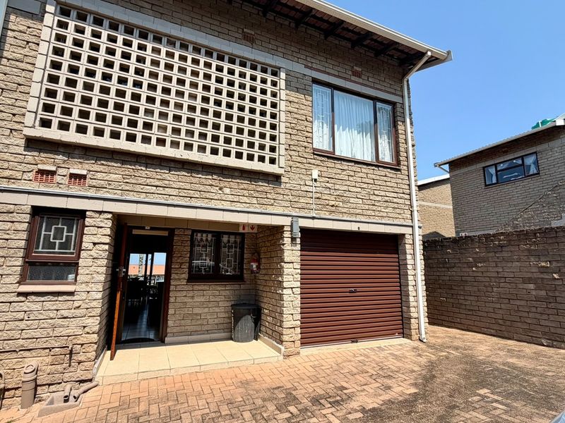 Front elevation of a townhouse featuring a brick facade, concrete breeze block detailing, a single roller garage door, and a paved driveway entrance.